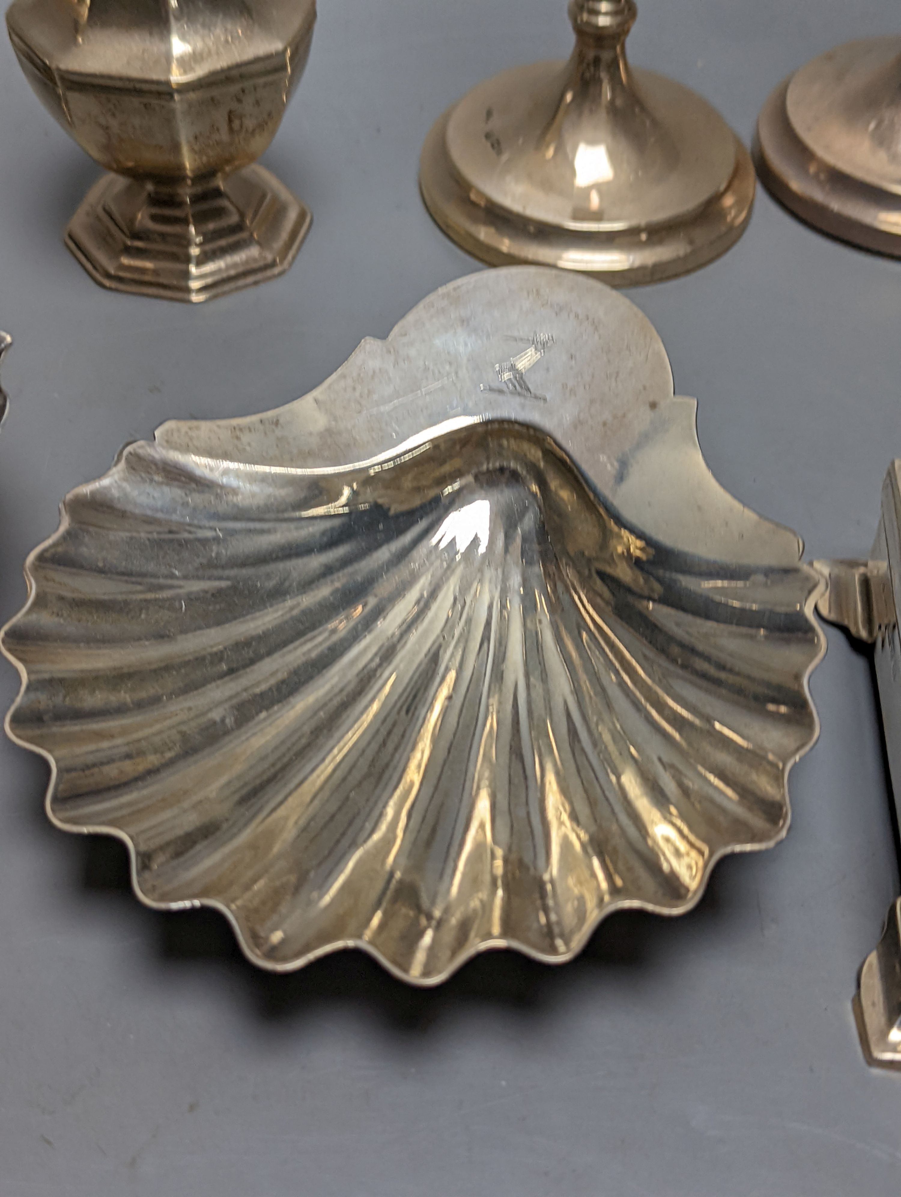A mixed collection of silver to include a George III silver butter shell, London, 1799, a small cigarette box, two casters, a pair of slender candlesticks (loaded) and two small bowls including white metal